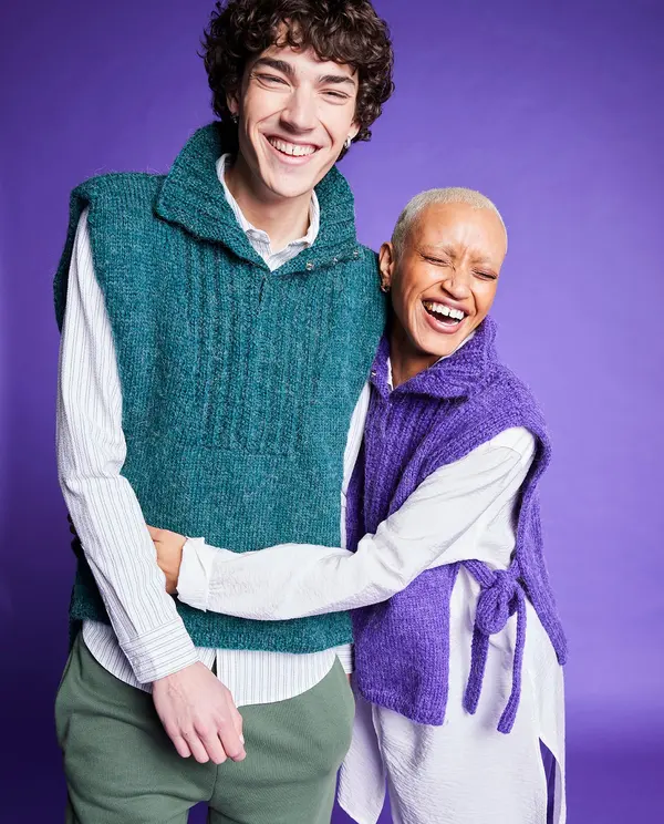 Dois modelos vestem camisolas de malha sem mangas em cores verde água e lilás, ambos sorrindo com fundo roxo.