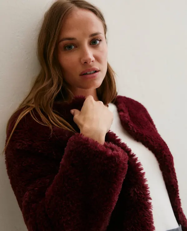 Casaco feminino felpudo vinho com blusa branca contra parede branca