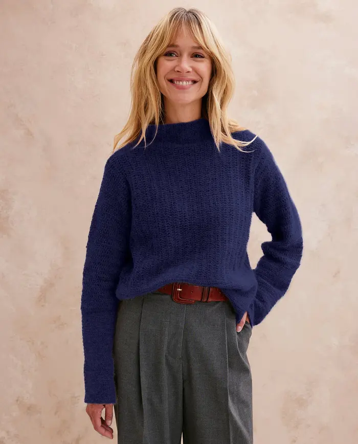 Mulher sorridente com camisola azul escura de malha e calças cinzentas
