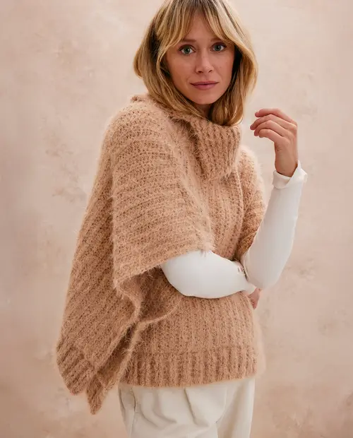 Poncho de malha bege com gola alta e textura felpuda numa modelo feminina