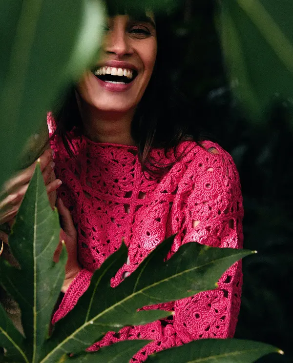 Mulher com camisola rosa feita de croché entre folhas verdes