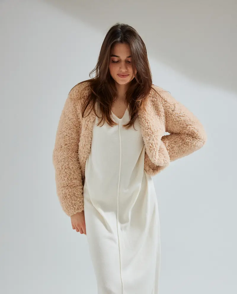 Casaco curto de pelo sintético bege claro com vestido branco.