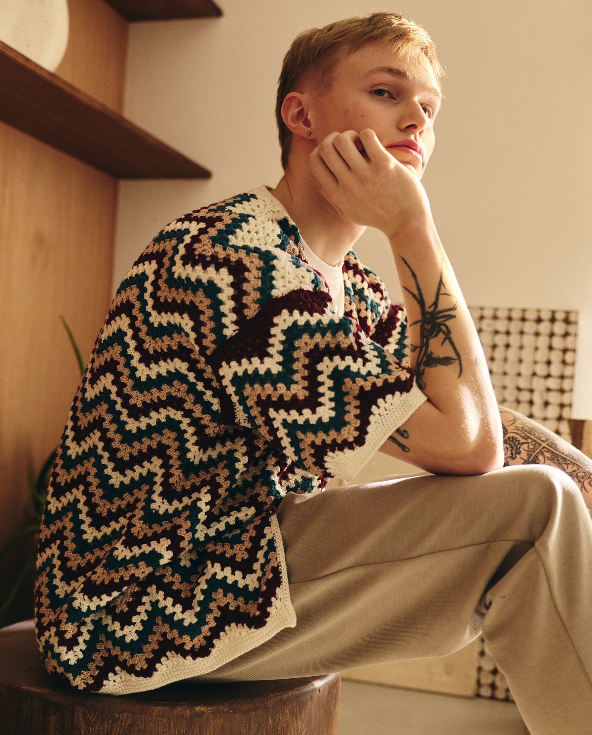 Jovem com camisola de malha crochetada padrão zig-zag colorido sentado num banco de madeira