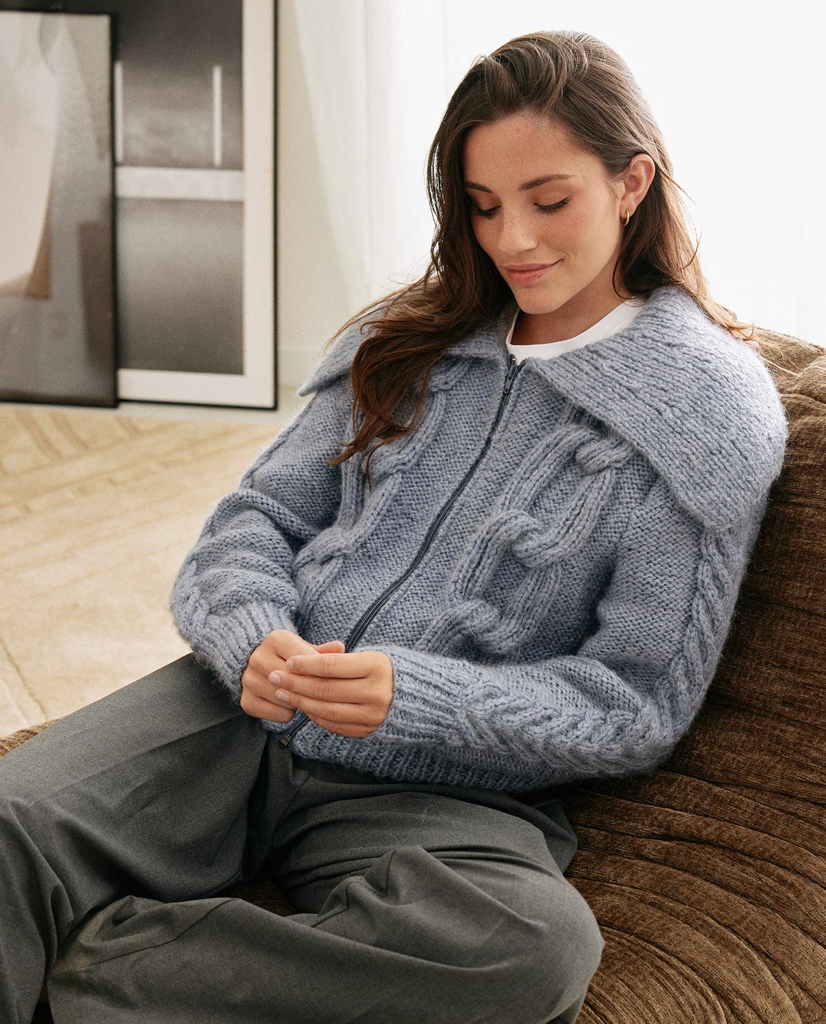 Mulher com casaco de malha azul cinza sentado num sofá castanho