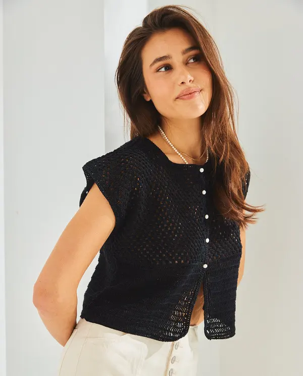 Mulher com colete de malha preto com botões brancos e calças brancas