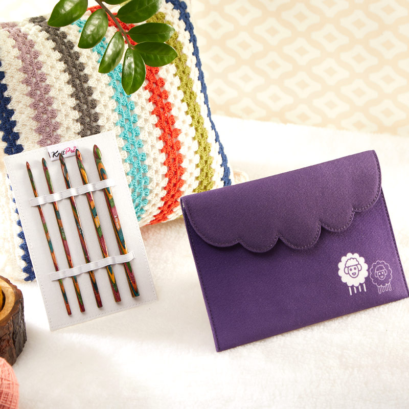 Conjunto de agulhas de tricô coloridas com bolsa roxa decorada com ovelhas, almofada colorida ao fundo