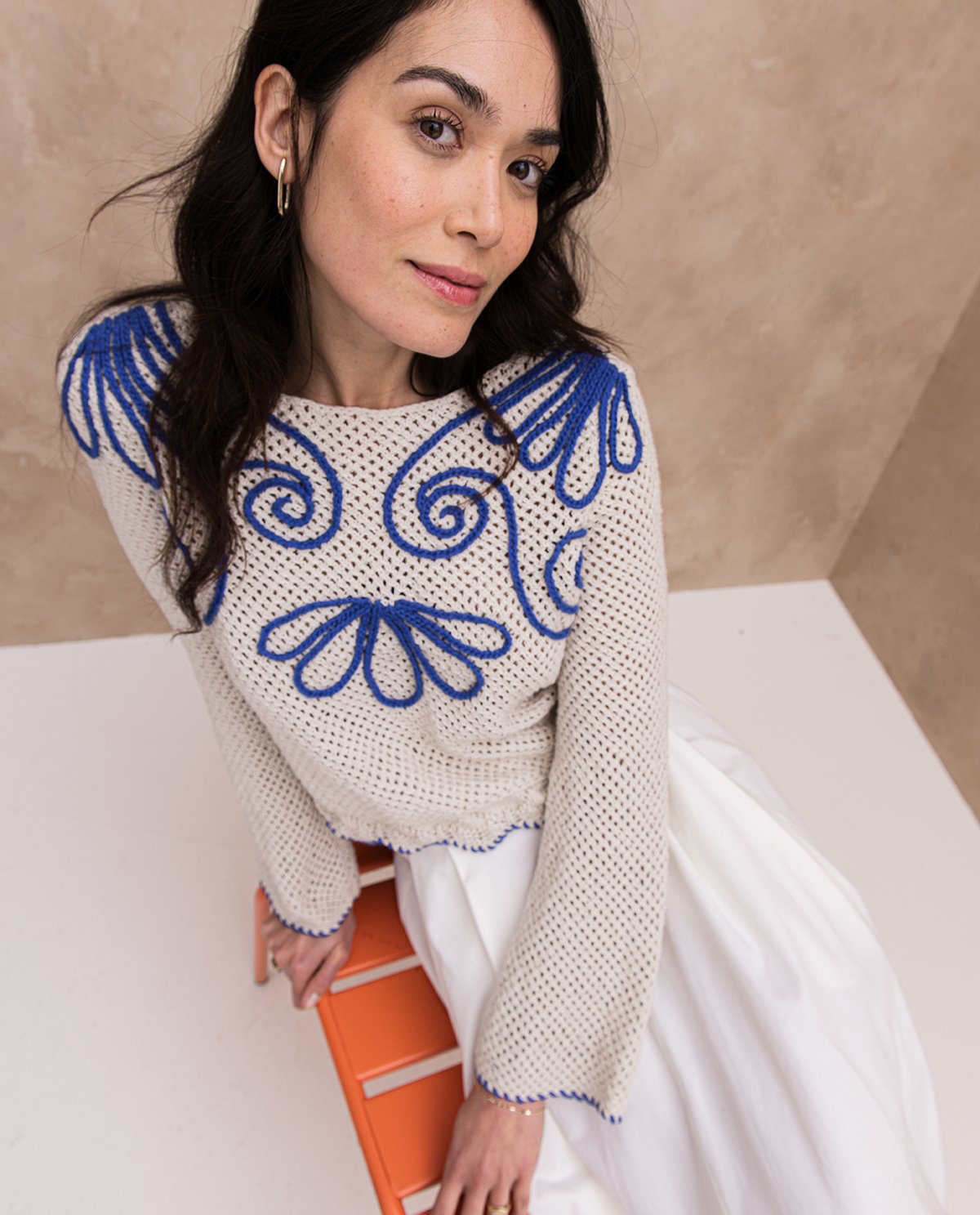 Mulher com camisola bege e azul sentada numa cadeira laranja