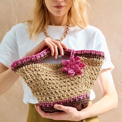 Bolsa trançada bege com rosa e castanho segurada por mulher com camisa branca