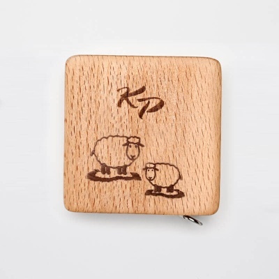 Caixa quadrada de madeira clara com gravura de ovelhas e as letras 'KD'