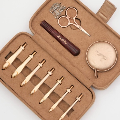 Conjunto de ferramentas de cuidado pessoal em estojo castanho claro com várias ferramentas douradas e utensílios para manicure.