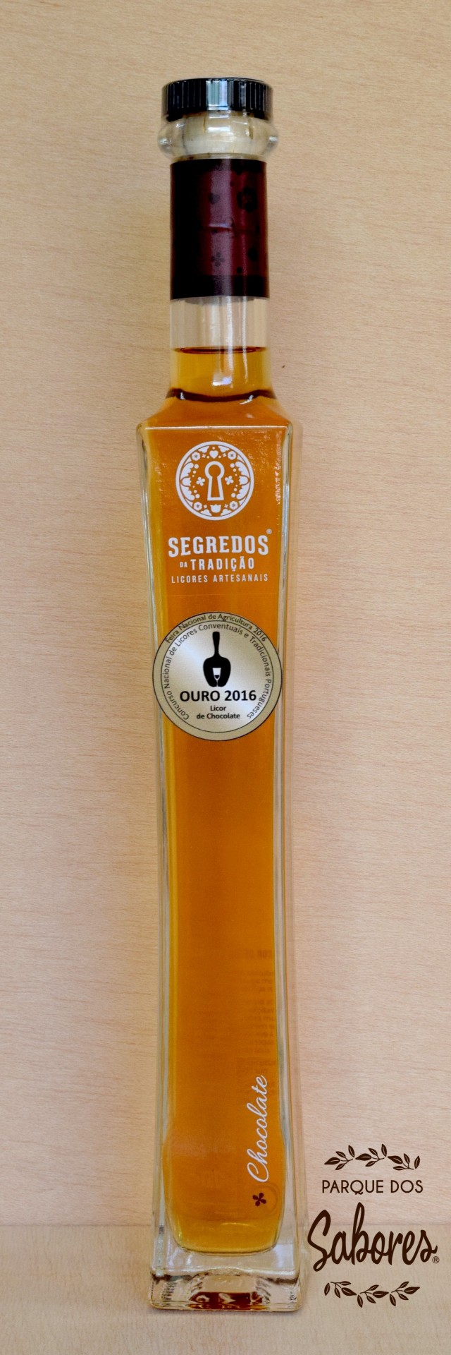 Licor de Chocolate Garrafa de licor artesanal âmbar com rótulos e tampa preta sobre madeira
