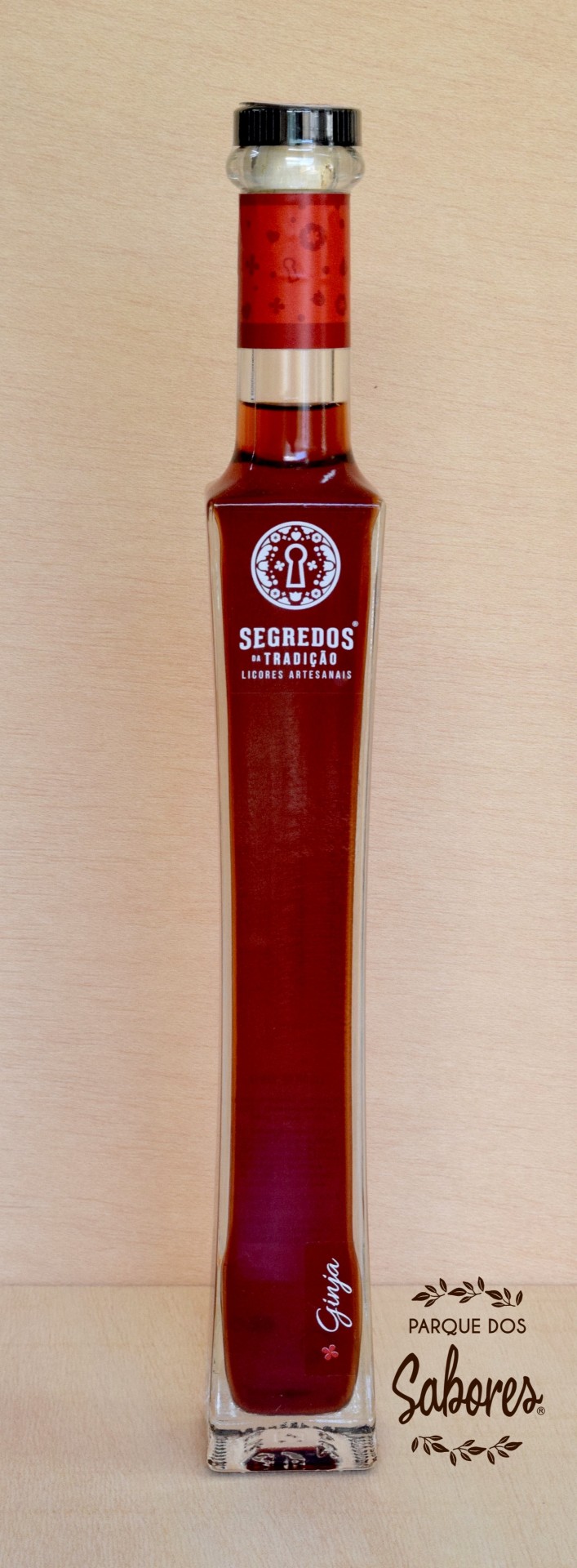 Licor de Ginja Garrafa alta de licor artesanal vermelha com tampa preta e rótulo branco