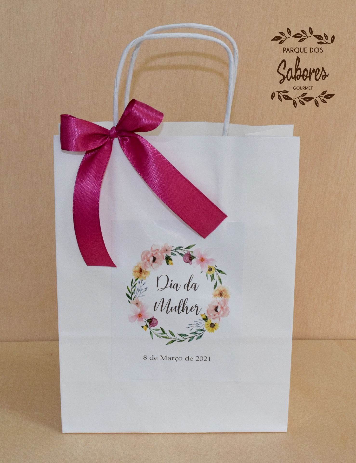 Saco de papel branco com laço rosa escuro e etiqueta 'Dia da Mulher 8 de Março de 2021'