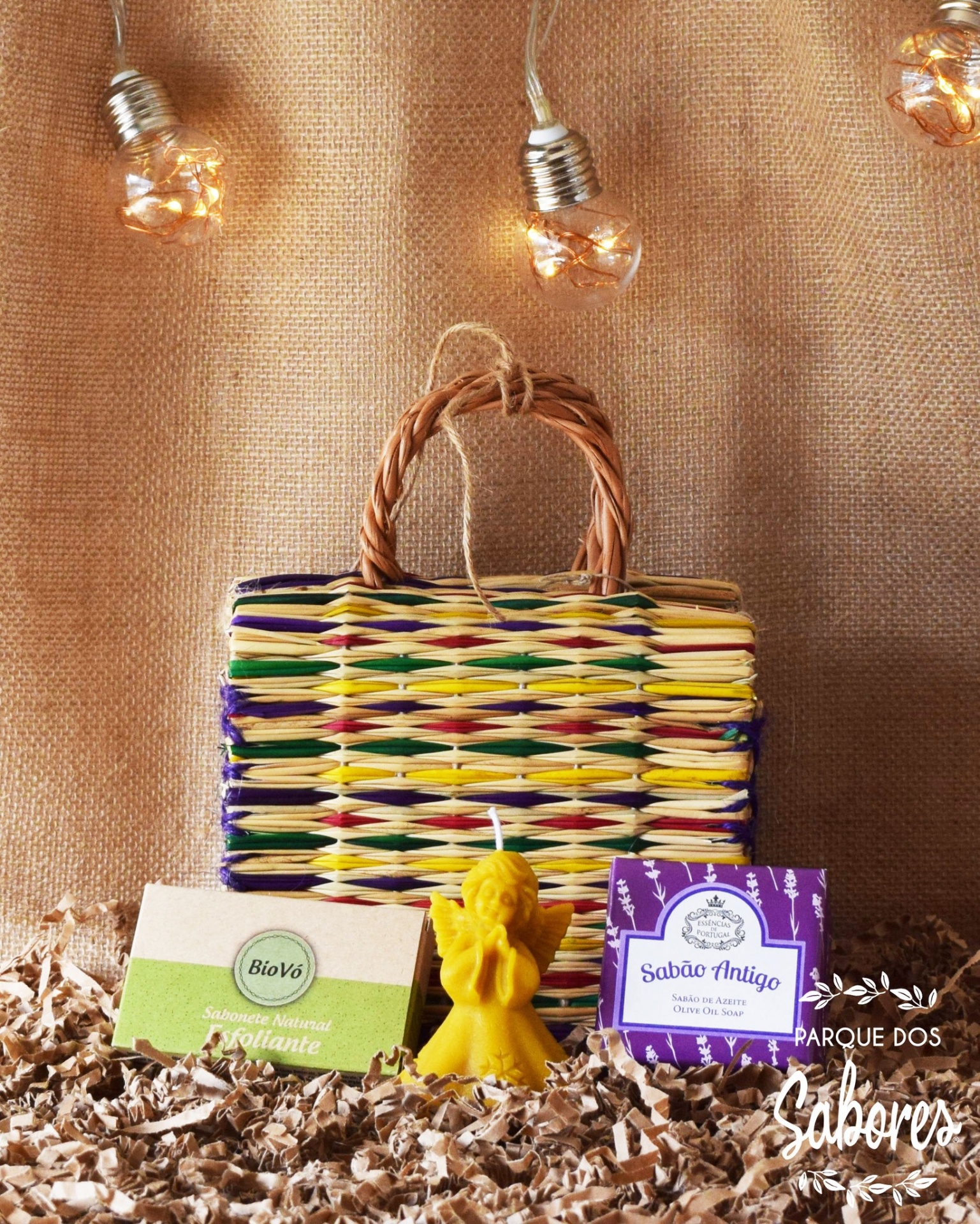 Cesto trançado colorido com vela amarela e duas caixas de sabão em fundo decorativo