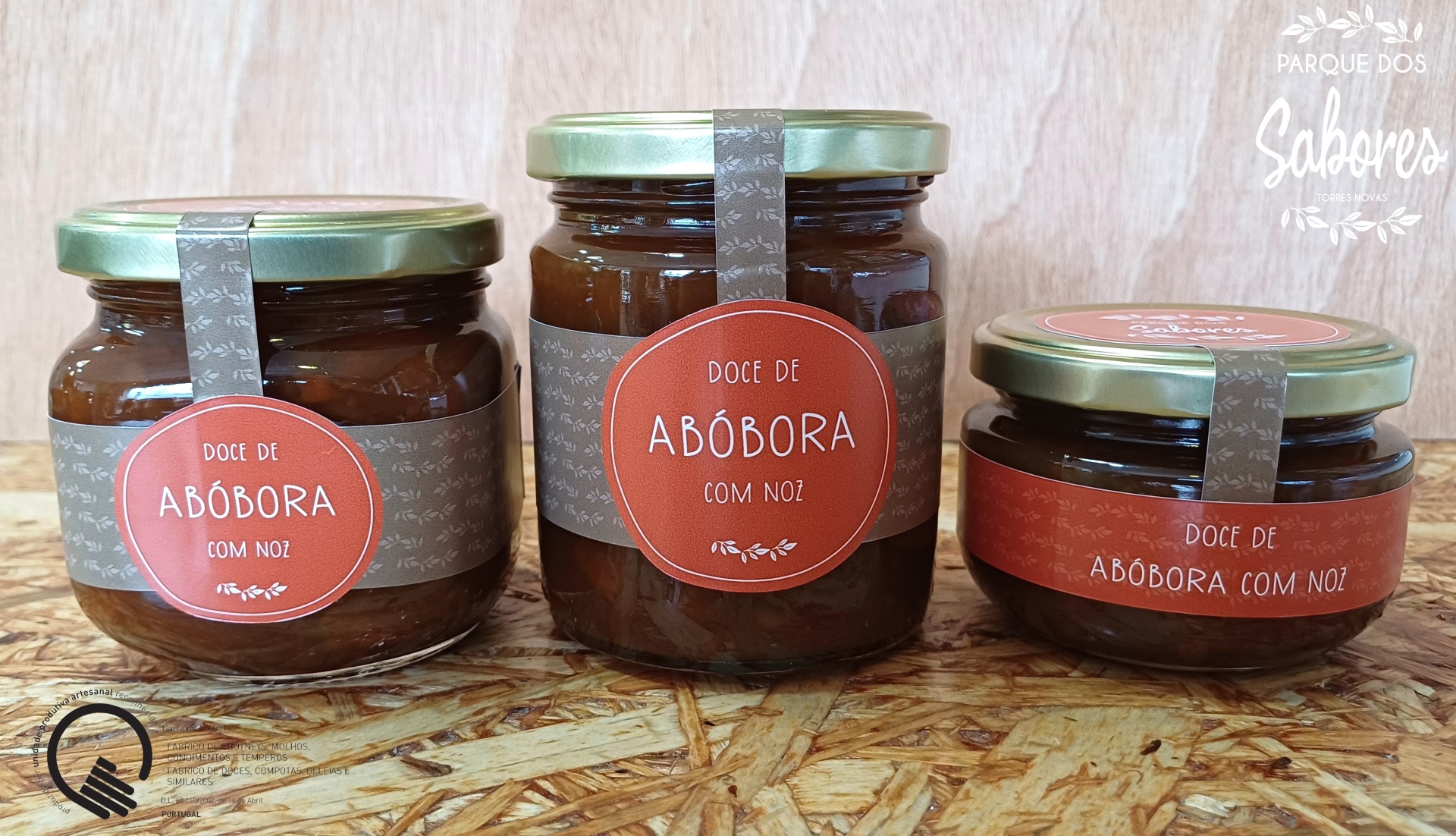 Três frascos de vidro com doce de abóbora com noz com etiquetas castanhas e laranja sobre superfície de madeira clara