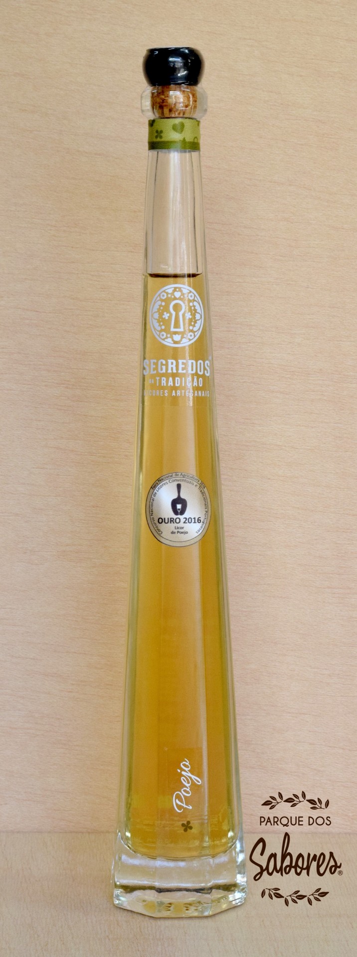 Licor de Poejo Garrafa alta e estreita de licor amarelo claro com rótulos e selo de premiação sobre fundo de madeira