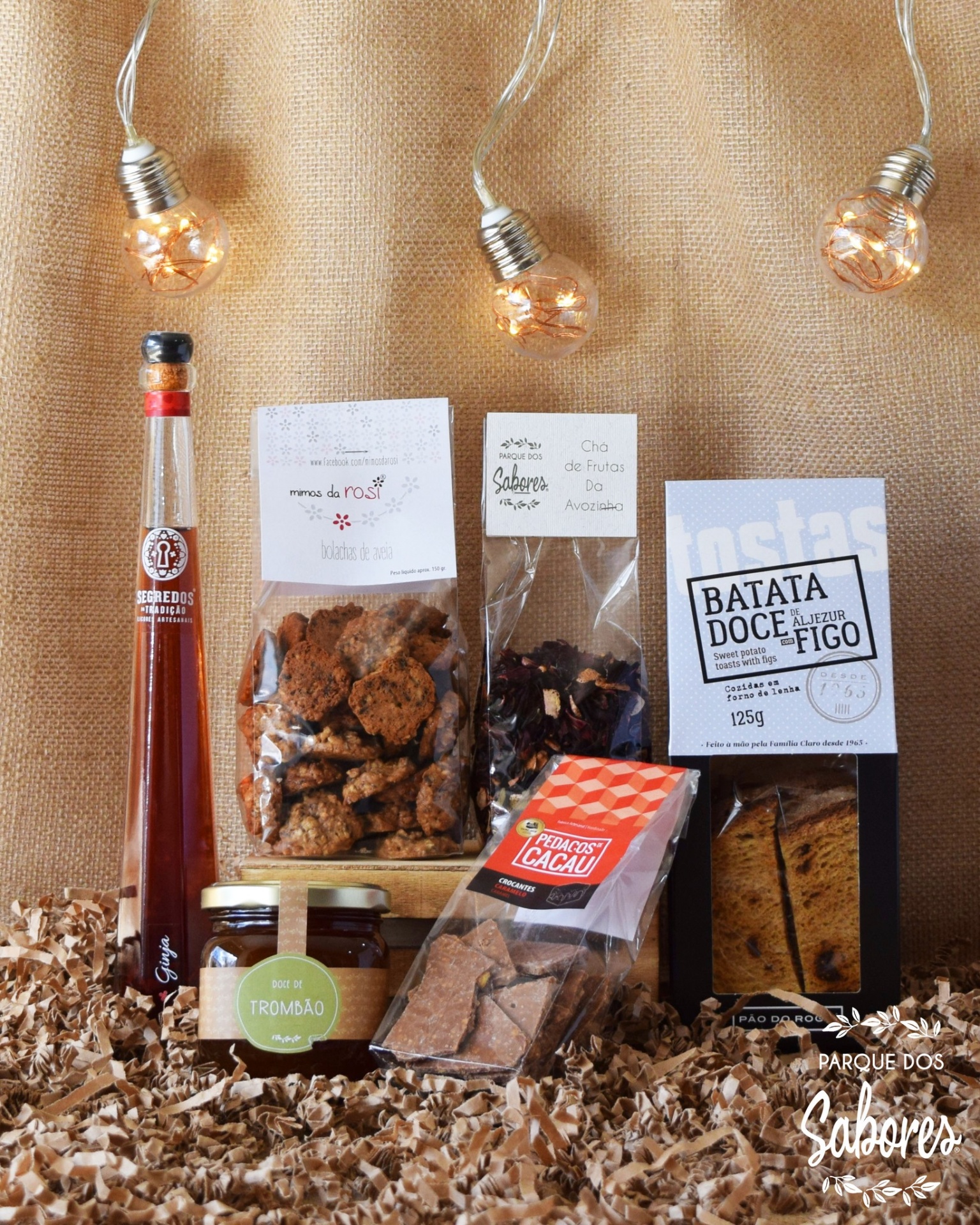 Produtos alimentares artesanais dispostos sobre aparas de madeira com lâmpadas decorativas e fundo em tecido bege