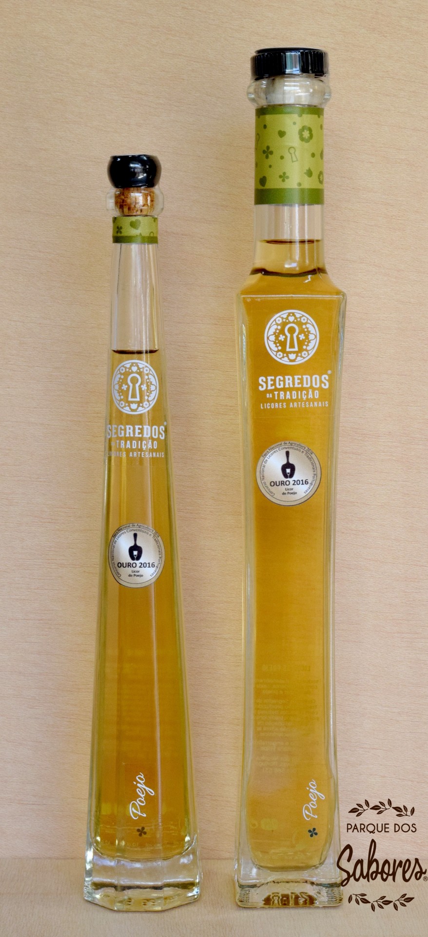 Dois frascos altos de licor amarelo com rótulos verdes e texto branco, sobre fundo de madeira clara.