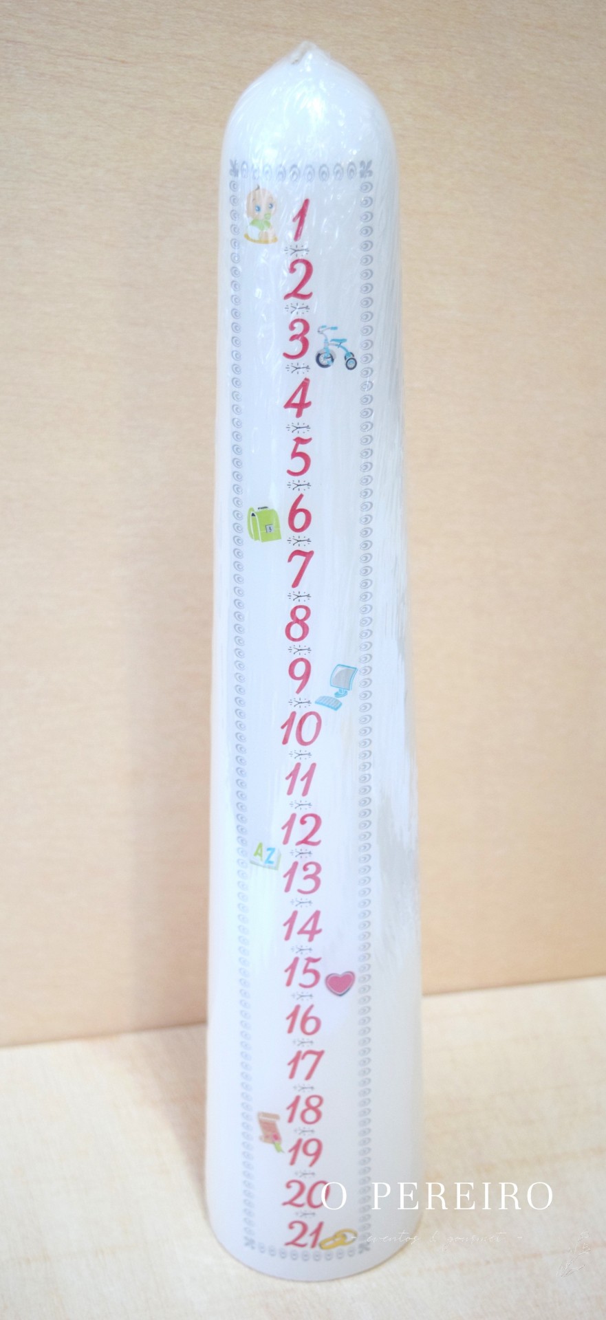 Vela branca alta com números vermelhos e desenhos coloridos em fundo de madeira clara.