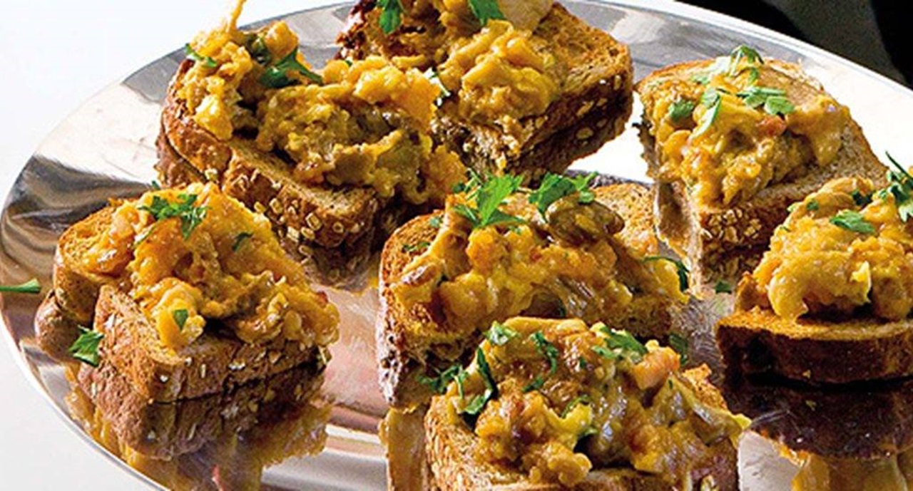 Tostas de pão integral com mistura cremosa alaranjada e ervas verdes num prato de metal