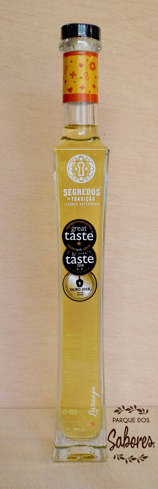 Licor de Laranja Garrafa de licor amarelo com rótulos, sobre fundo de madeira clara e logo Parque dos Sabores