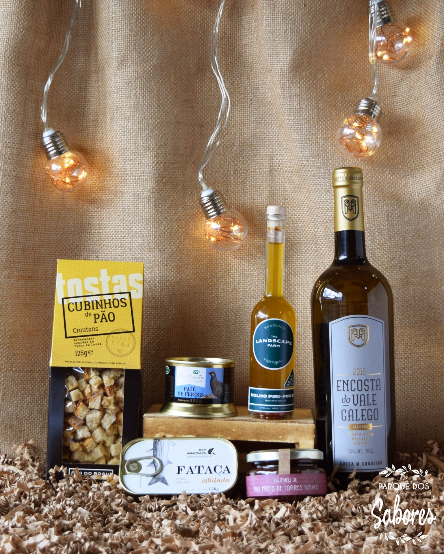 Produtos gourmet sobre aparas de madeira com vinho branco e luzes decorativas