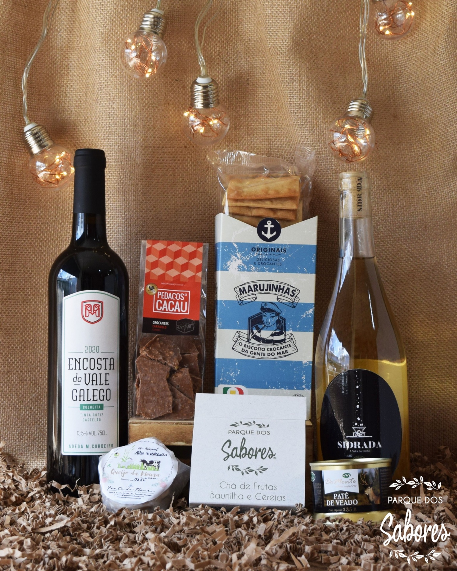 Produtos gourmet com vinho, bolachas, chocolate e chá em fundo de juta com luzes decorativas