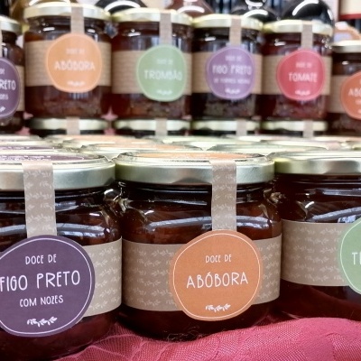 Frascos de vidro com doces variados com rótulos coloridos em cima de tecido vermelho