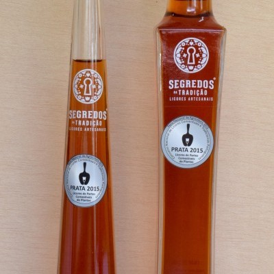 Duas garrafas altas de licor cor âmbar com rótulos brancos e tampa preta