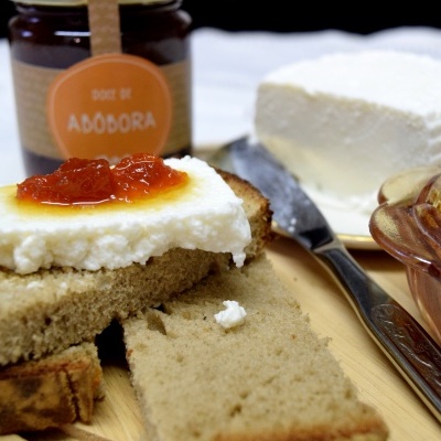 Pão com queijo cremoso e doce de abóbora em tábua de madeira com frasco e bloco de queijo ao fundo