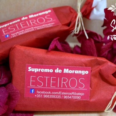 Três produtos embrulhados em papel vermelho com etiqueta 'Supremo de Morango ESTEIROS' e folhas decorativas vermelhas