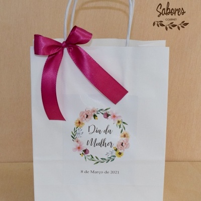 Saco de papel branco com laço rosa escuro e etiqueta 'Dia da Mulher 8 de Março de 2021'