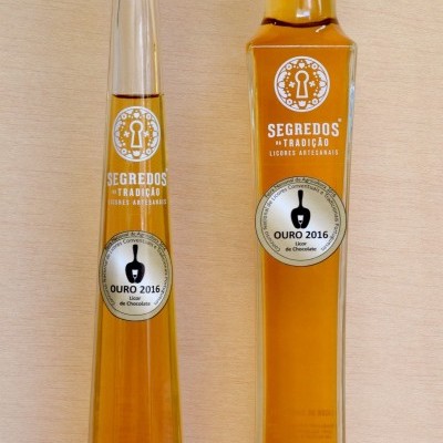 Duas garrafas altas de licor artesanal âmbar com rótulos SEGREDOS DA TRADIÇÃO e OURO 2016