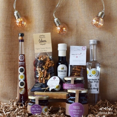 Produtos alimentares variados em frascos e embalagens com figos secos, azeite e doces, fundo tecido castanho e luzes decorativas