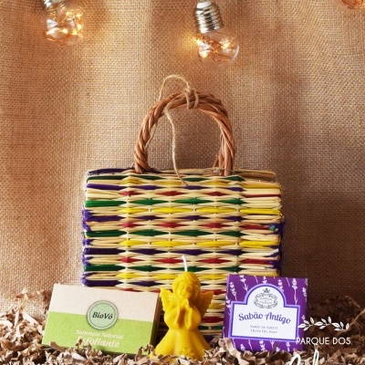 Cesto trançado colorido com vela amarela e duas caixas de sabão em fundo decorativo