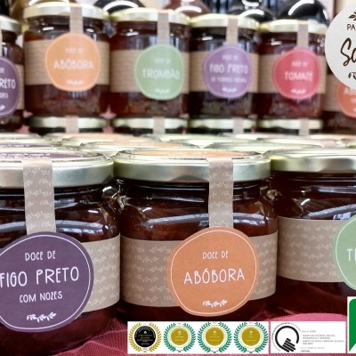 Frascos de compotas com etiquetas coloridas e tampas metálicas sobre tecido vermelho.