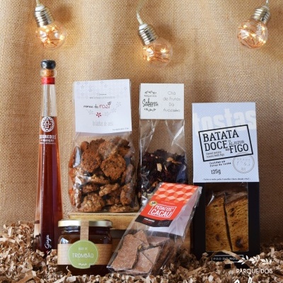 Produtos alimentares artesanais dispostos sobre aparas de madeira com lâmpadas decorativas e fundo em tecido bege