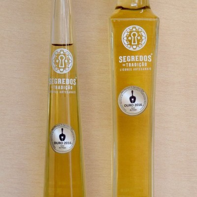 Dois frascos altos de licor amarelo com rótulos verdes e texto branco, sobre fundo de madeira clara.