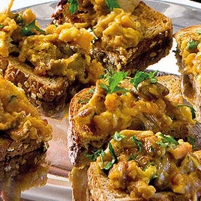 Tostas de pão integral com mistura cremosa alaranjada e ervas verdes num prato de metal