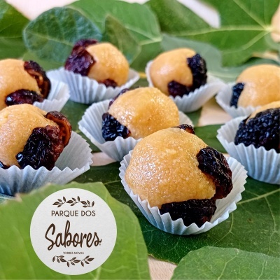Doces tradicionais com pedaços escuros em forminhas brancas sobre folhas verdes com selo 'PARQUE DOS Sabores TORRES NOVAS'.
