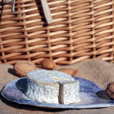 Queijo branco redondo numa tábua azul com nozes e cesta de verga ao fundo
