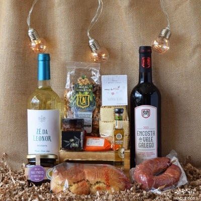 Conjunto de produtos gourmet com vinhos, nozes, queijo, patê, azeite, broa e chouriço sobre fundo de juta com luzes decorativas