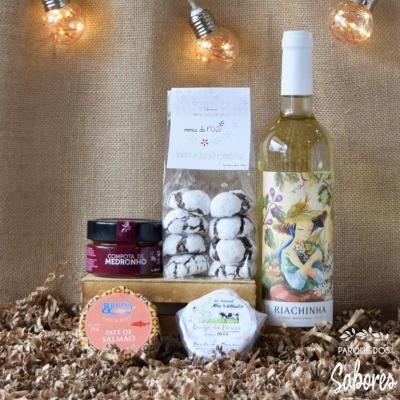 Conjunto gourmet com vinho branco, bolachas de noz, compota de medronho, paté de salmão e queijo sobre fundo de juta com luzes decorativas.