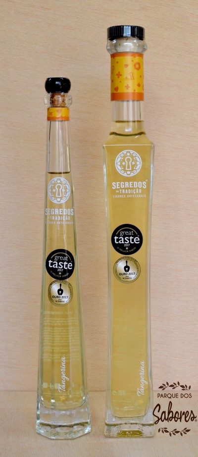Duas garrafas de licor artesanal Tangerina com rótulos de prémios sobre fundo de madeira clara