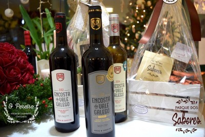 Três garrafas de vinho Encosta do Vale Galego ao lado de flores e cabaz de produtos embalados