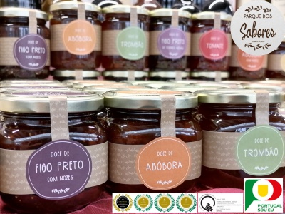 Frascos de compotas com etiquetas coloridas e tampas metálicas sobre tecido vermelho.