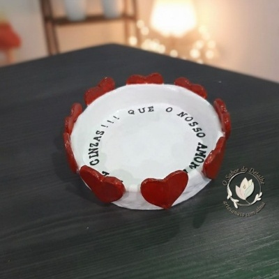 Cinzeiro branco com corações vermelhos e texto interno sobre uma mesa escura