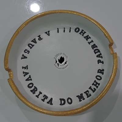 Parte superior de uma peça cerâmica branca com borda dourada e texto preto em círculo