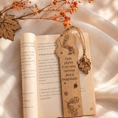 Marcador de páginas artesanal com folhas desenhadas e cordão rústico sobre livro aberto e flores secas