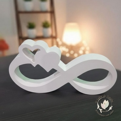 Objeto decorativo branco em forma de infinito com corações sobre superfície preta